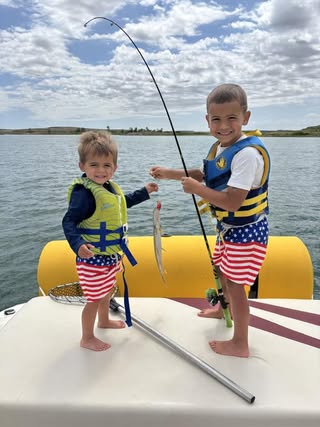 Two young anglers in life jackets showing off their catch on a boat